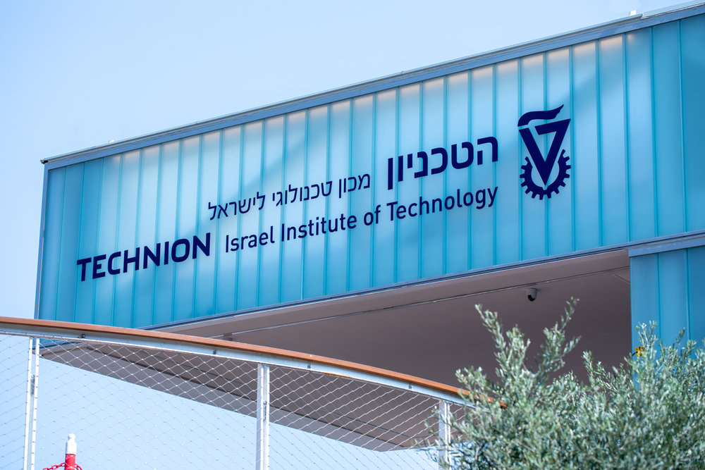 ‘“Facade of a building with signage in Hebrew and English. The Hebrew text reads ‘Technion Israel Institute of Technology’ and the English text is the same. The Technion logo, a stylized letter ‘T’, is visible between the lines.”