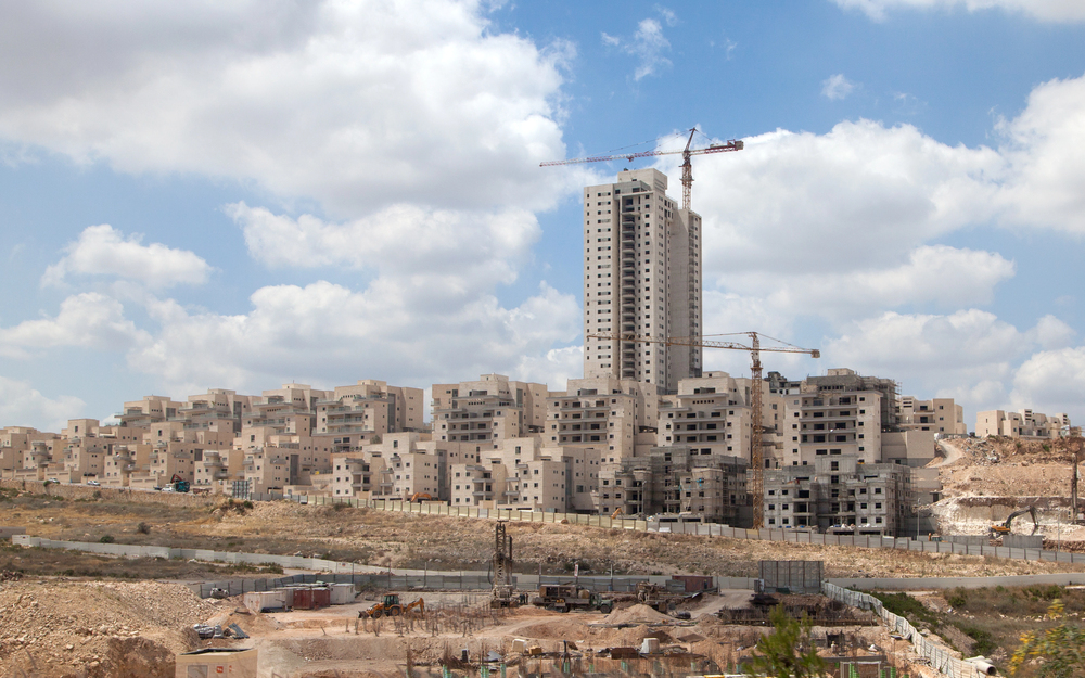 The image shows a construction site with multiple buildings in various stages of completion. There are several cranes positioned around the site, indicating ongoing construction work.