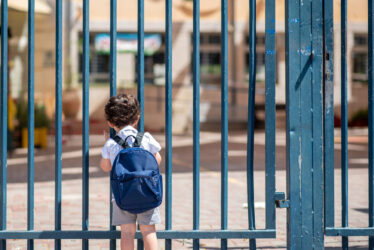 Child with bag back to school near closed gate
