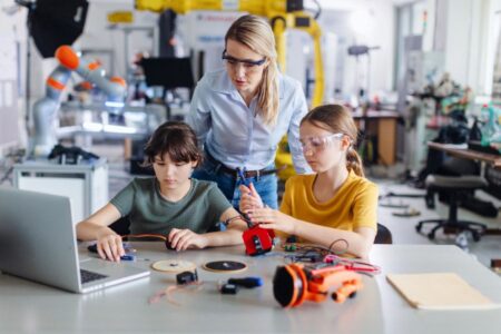 Female teacher helping to girls working on small robot, building robotic car in after-school robotics club. Children learning robotics in Elementary school. Girls in science.